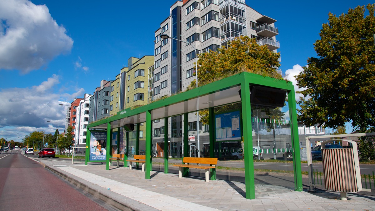 Busshållplats med gröna väderskydd vid Almbyplan.