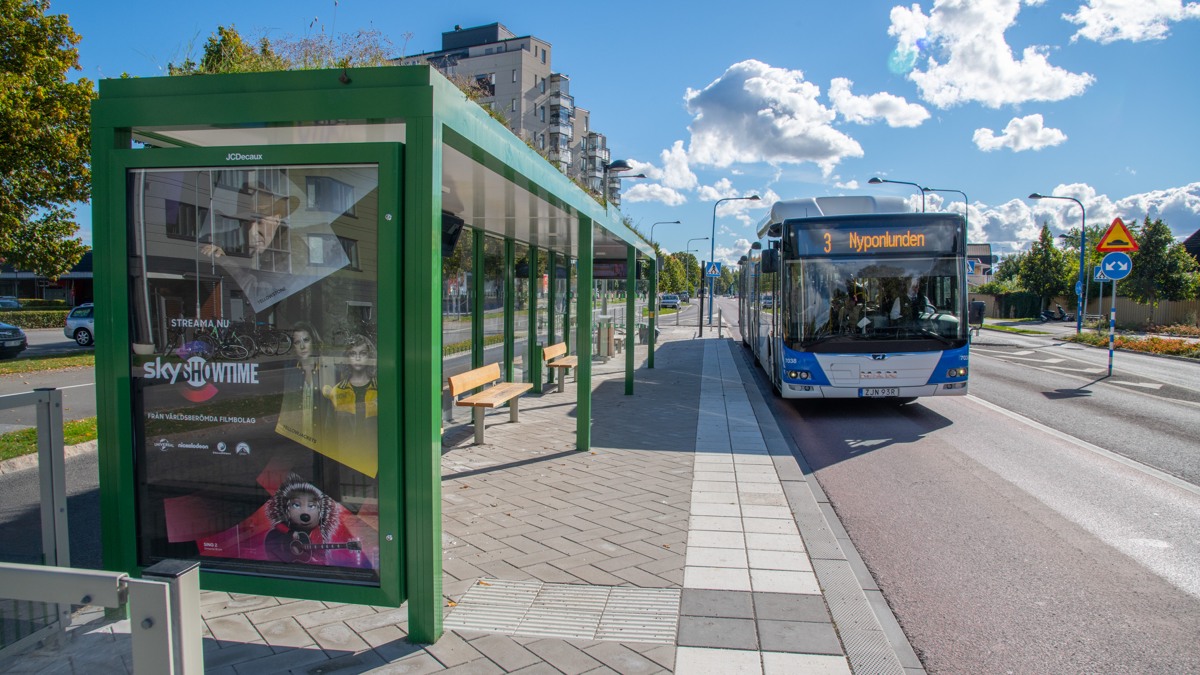 En buss anländer vid en hållplats med det gröna väderskyddet, som är karakteristiskt för det nya kollektivtrafiksystemet med snabbussar.