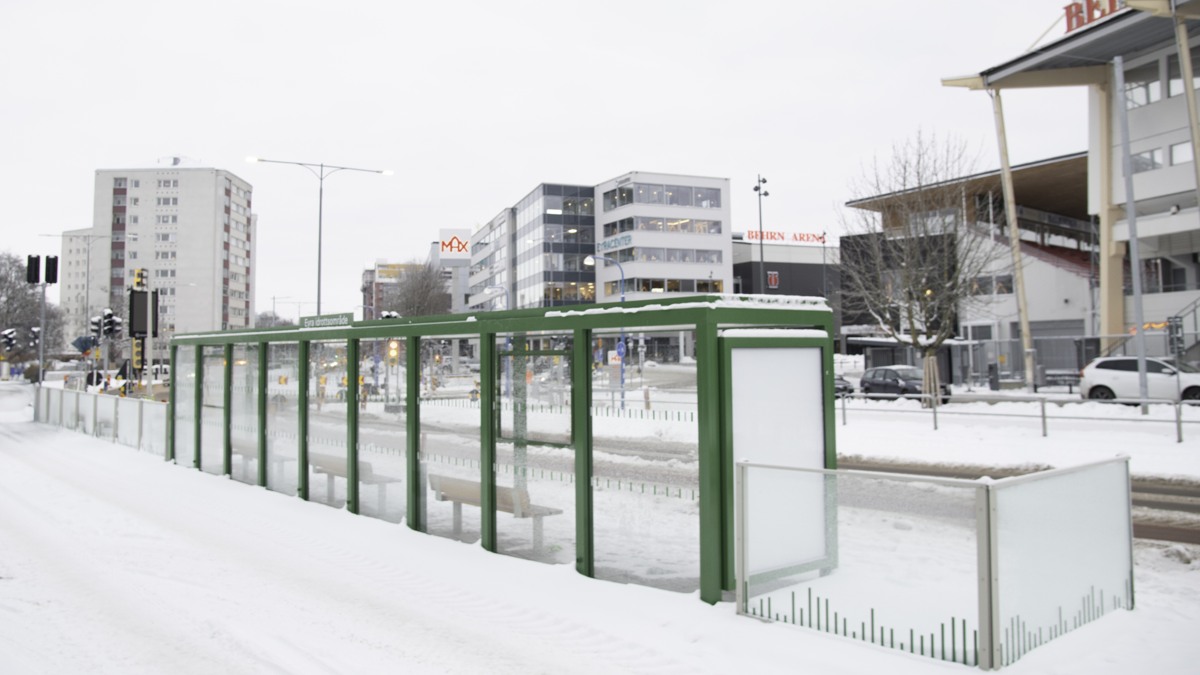 Mittförlagd busshållplats med grönt väderskydd och Behrn Arena i bakgrunden.