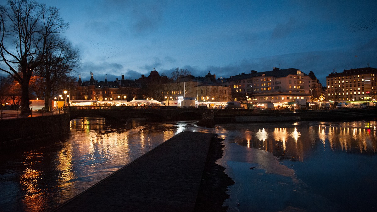 Kvällsvy över vattnet med stadssiluett och marknaden med lampor. 