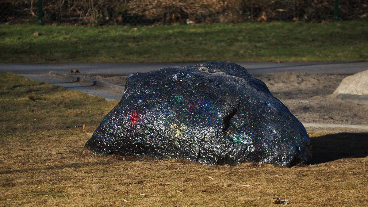 Svart, glittrande sten omgiven av gräs.