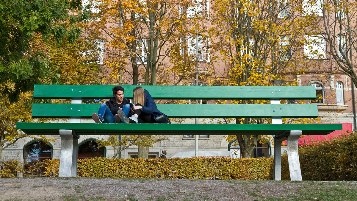 Huge green park bench where two people sit.