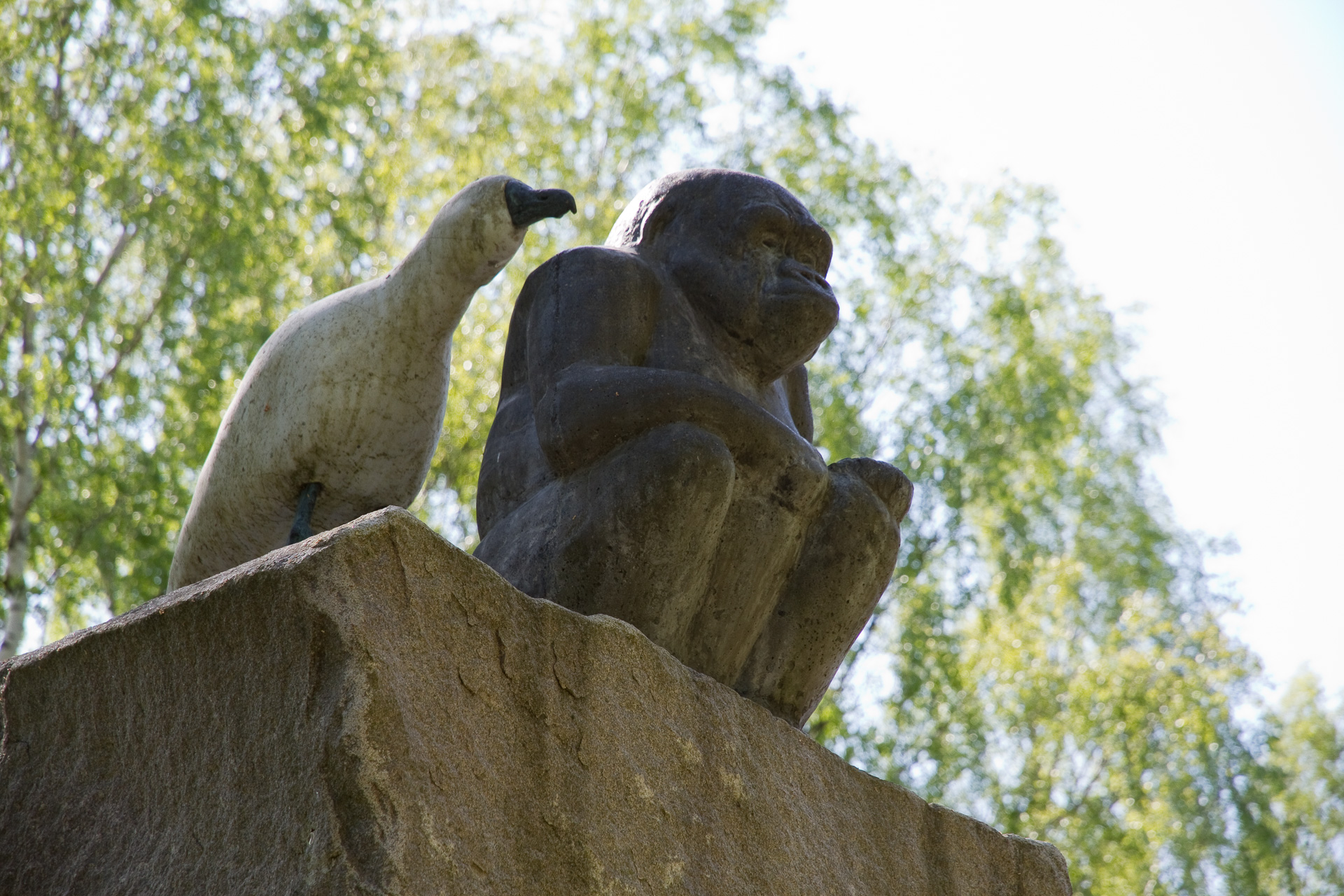 På en hög sockel av granit sitter en liten gorilla på huk med de långa armarna i knät och tittar ut över parken. Bakom den på samma sockel står två trutar uppflugna. Trutarna