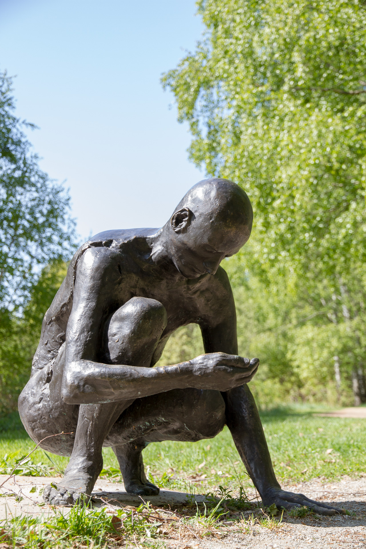 Sculpture of a man in concrete and bronze who is kneeling and has picked up something from the ground.