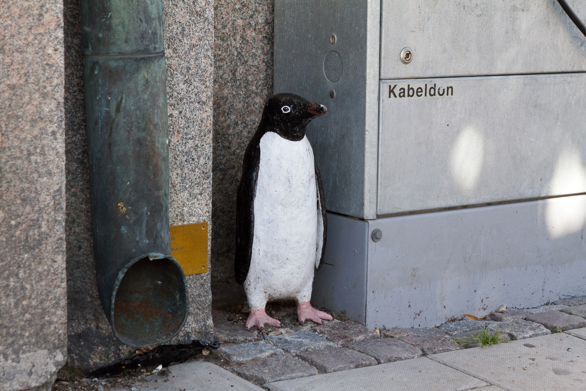 En liten pingvin stående dold bredvid ett elskåp.