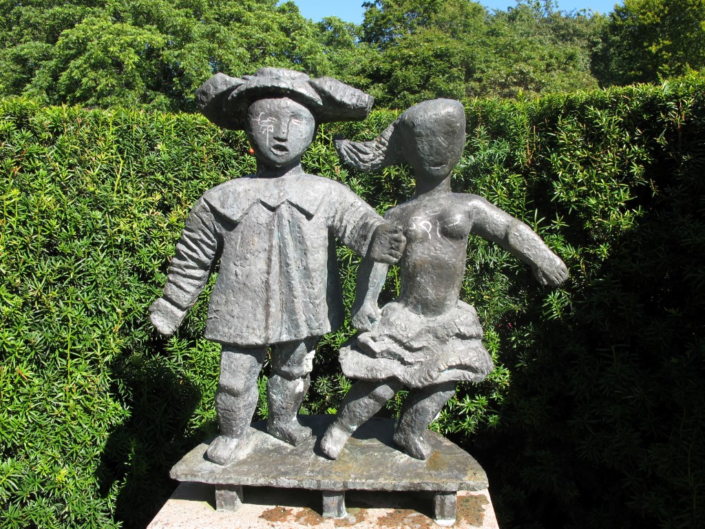 Två figurer i brons - en man med bred hatt och en kvinna med tofs och kjol.