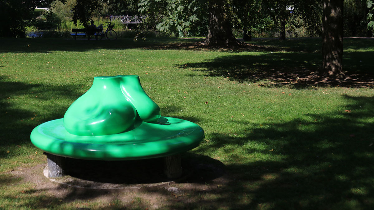 A broad green soft circular shape standing on four stumps. On the green shiny shape are two bumpy shapes.
