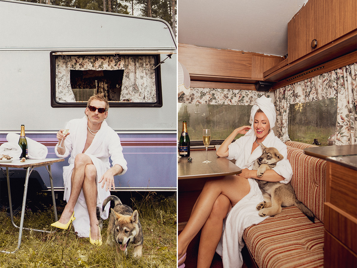 Man i badrock med champagneflaska och hund utanför husvagn och kvinna i morgonrock med champagneflaska och hund inne i husvagn
