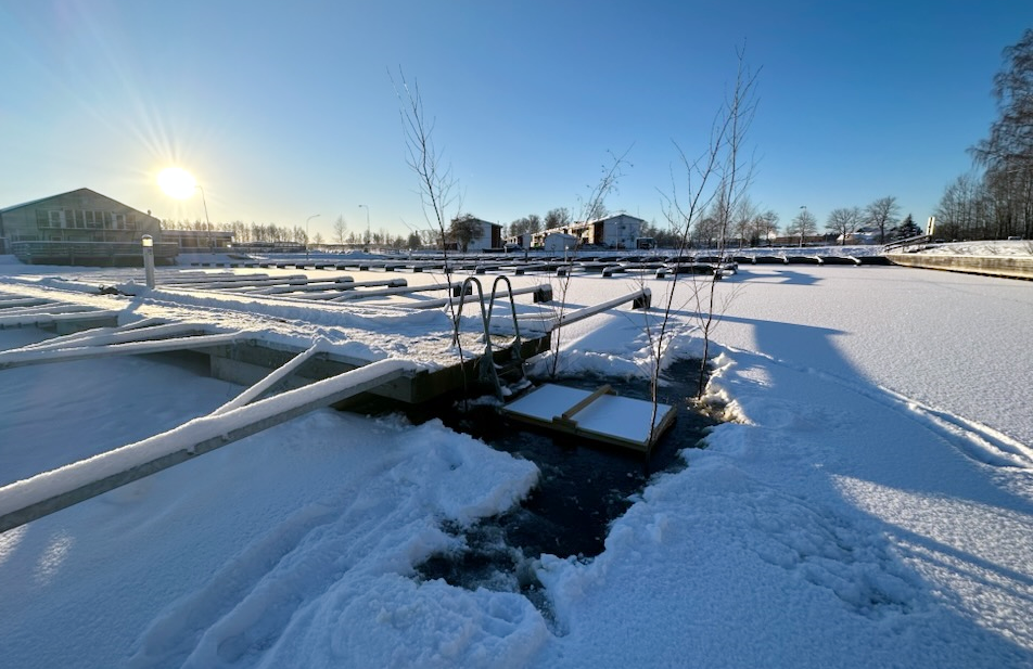 Snöbeklädd hamn med öppen isvak vid bryggan. Vaken har grenar för markering så ingen ska ramla i av misstag.