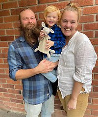 En man med skägg och en glad kvinna som tillsammans håller i ett barn.